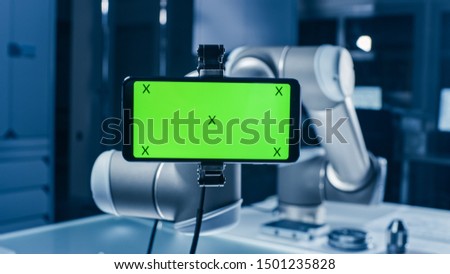 Robot Arm Holding Green Mock-up Screen Smartphone in Landscape Mode. Industrial Robotic Manipulator End Effector Holds Mobile Phone with Chroma Key Display. Royalty-Free Stock Photo #1501235828