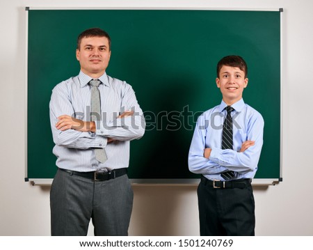 Portrait of a man and boy dressed in a business suits near blackboard background - learning and education concept