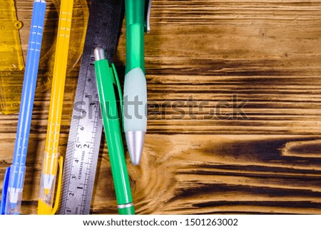 Multi colored ball pens, protractor and ruler on rustic wooden table. Top view