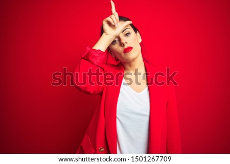 Young beautiful business woman standing over red isolated background making fun of people with fingers on forehead doing loser gesture mocking and insulting.
