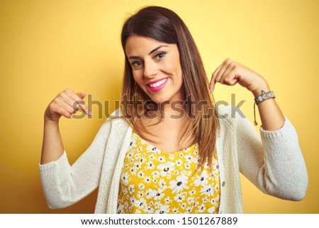 Young beautiful woman wearing jacket standing over yellow isolated background looking confident with smile on face, pointing oneself with fingers proud and happy.