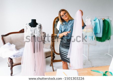 Attractive stylish seamstress or clothing designer measuring a length of neutral colored fabric alongside her sewing machine with copyspace