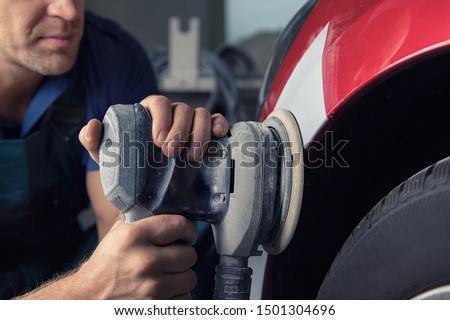 A man who sanding with a grinder and prepares the paint for the car in a car service. Royalty-Free Stock Photo #1501304696