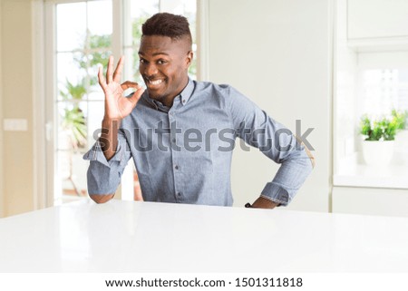 Handsome african american man on white table smiling positive doing ok sign with hand and fingers. Successful expression.