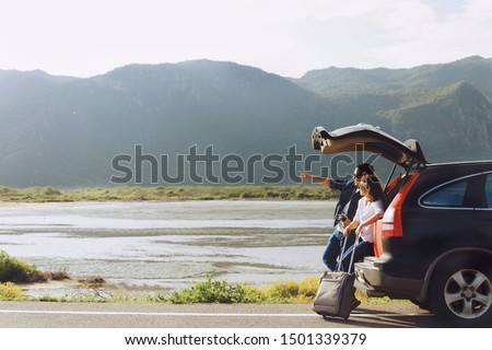Two Asian people sitting on car truck,they’re looking at the Mountain View and take a picture.