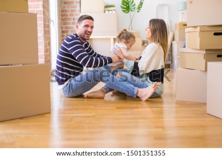 Beautiful family sitting on the floor playing with his kid at new home around cardboard boxes