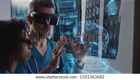 Medium close-up of a male and a female doctor examining 3D brain hologram while wearing VR headsets