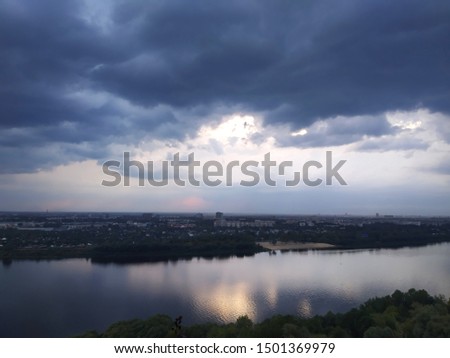 Dark clouds before a thunderstorm over a river paysage. the sun shines from below the clouds personifying a ray of hope and happy days after the storm