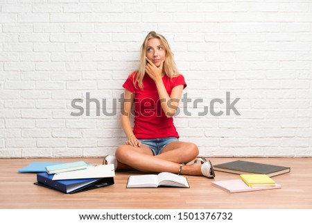 Young blonde student girl with many books on the floor thinking an idea