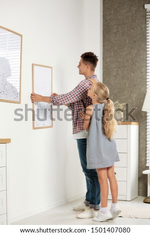 Father and daughter hanging picture on wall at home