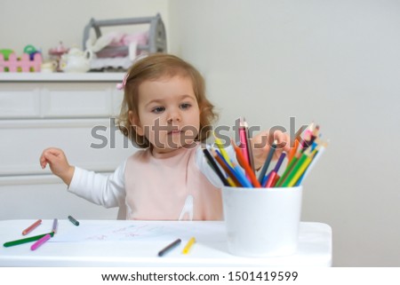 Cute baby girl is drawing picture with pencil at home. Beautiful child draws in kindergarten or preschool. Toddler Having Fun in nursery with nordic stylish.