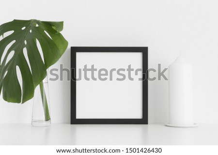 Black square frame mockup with a monstera leaf in a glass vase and a candle  on a white table.