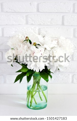 Bouquet of white peonies in a glass vase on a white break wall background with copy space