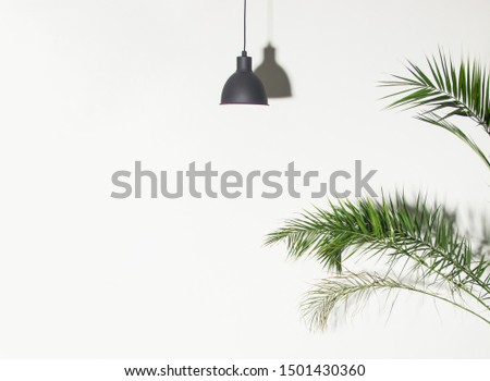 black minimal lamp chandelier with shadow in center of white wall background with green plant palm branches, minimal concept, free space on left side, place for text