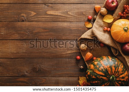Autumn composition. Pumpkins, blanket, fallen leaves, apples, red berries, walnuts on wooden table. Happy Thanksgiving concept. Flat lay, top view, copy space