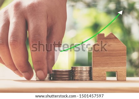Hand of people putting coin on house model with coins stack on wood table and bokeh natural background. Concept bitcoin for real estate investment.