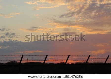 A beautiful colorful sunset over the hills with fluffy clouds and wire fence