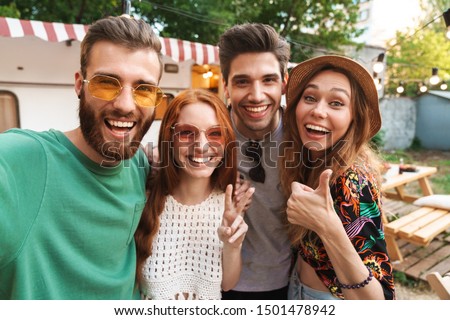Group of cheerful excited friends standing at the trailer outdoors, taking a selfie