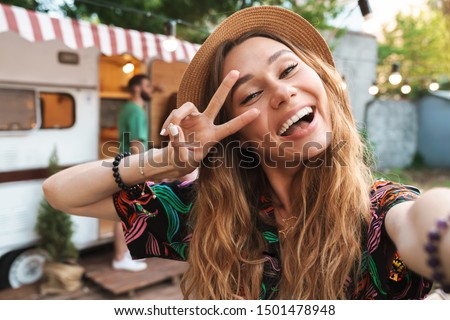 Cheerful young girl taking a selfie while standing at the campsite with a trailer on a background