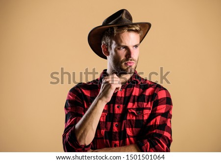 Handsome bearded macho. American cowboy. Beauty standard. Example of true masculinity. Cowboy wearing hat. Western life. Man unshaven cowboy beige background. Unshaven guy in cowboy hat.