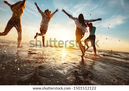 Four happy friends at sunset beach party runs to water Royalty-Free Stock Photo #1501512122