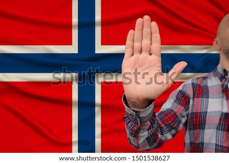 male hand with a gesture of protest, oaths against the background of the silk national flag of Norway, the concept of denial and prohibition and prohibition, close-up, copy space