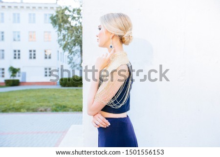 portrait of charming, lovely blond european girl in blue indian style dress with earrings looks to the side over white background outdoor..Bright makeup. Immersion different cultures concept