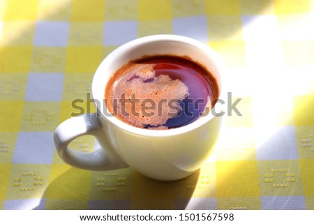 Cup of foamy morning coffee on a yellow tablecloth in the sunlight.