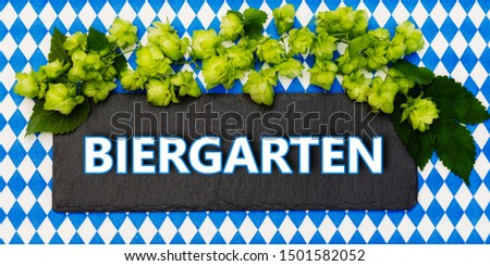 "Beer garden" word in german on black slate board with green hops. Oktoberfest background. October fest bavarian card.  Biergarten signboard in bavaria color