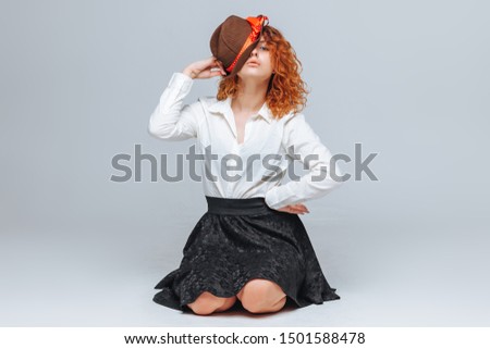 Red-haired joyful girl in a brown hat on a gray background in a white shirt