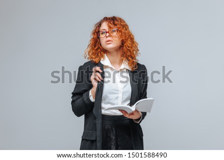 Red-haired woman in a black jacket and glasses read the white book