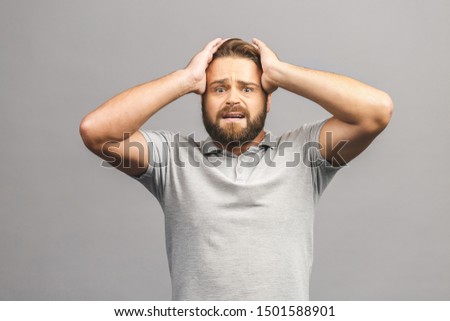 Upset unhappy young man in casual squeezing head with hands, suffering from headache. People, stress, tension and migraine concept isolated against grey background. 