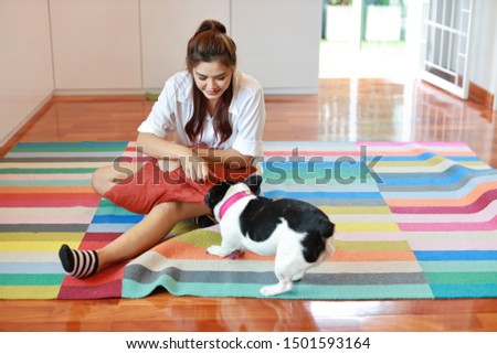 beautiful young asian woman wearing white shirt and holding red pillow who sitting and playing with her cute dog with happy and smiling face in living room. (lifestyle concept)