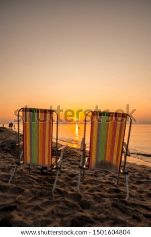 In the foreground are two sun chairs. The sun is singing in the sea. Concept: holiday or calendar and picture postcards