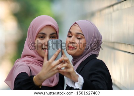 Two beautiful young Asian muslim girl taking selfie with using a smartphone and having fun. Selective focus image.