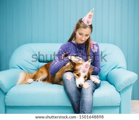 Beautiful young woman and a dog in holiday caps. They are sitting on a blue sofa.