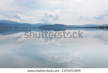 Blue cloudy sky reflected on water with mountains in the horizon