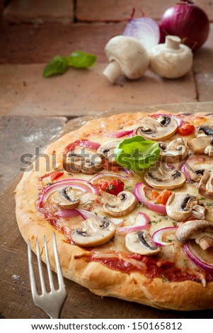 Delicious crisp crusty vegetarian pizza topped with mushrooms, onion, tomato and melted cheese on old weathered bricks with copyspace