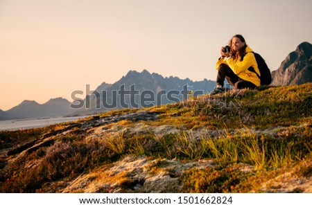 Happy girl traveler with a camera in his hands in Norway, on the Lofoten Islands admires the sunset on a background of mountains