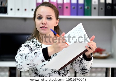 Business portrait of a pretty young woman secretary in the office in a light dress. Sitting, talking right in front of the camera in various poses.