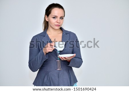 Portrait of a pretty female manager on a white background in a gray business suit with a cup of coffee in her hands. Standing right in front of the camera in various poses.