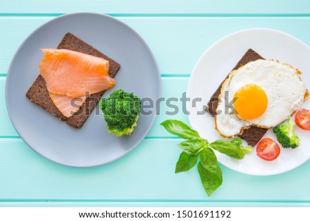 Delicious eggs with smoked salmon toasts with vegetables and greens on wooden turquoise background, top view. 