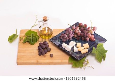 a bamboo board and a blue plate on which lie grapes , cheese and green leaves on a white background