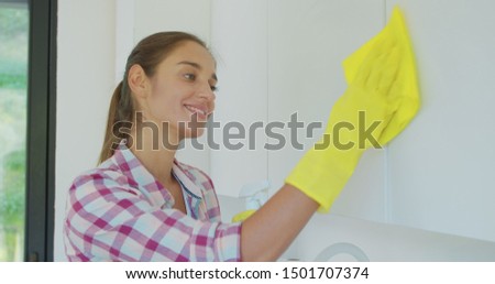 Woman's hand in a yellow rubber glove cleans the shiny surface of a modern plastic kitchen Cabinet with a cloth. The concept of spring cleaning and home work.