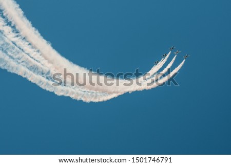 Fighter jets flying against a bright sky, performing figures turns from the smoke
