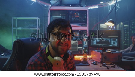 Medium shot of a young male hacker laughing then glaring into camera