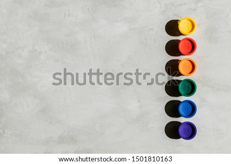 Action painting, trend art background. Multicolored paints in round jars and brush on a gray concrete background with copy space. Hard light.