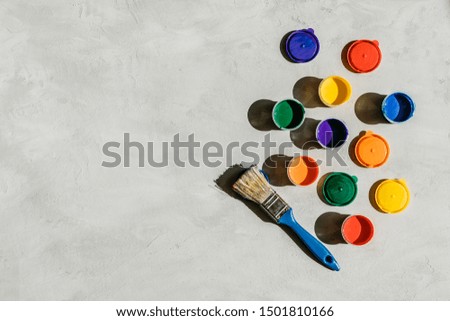 Action painting, trend art background. Multicolored paints in round jars and brush on a gray concrete background with copy space. Hard light.