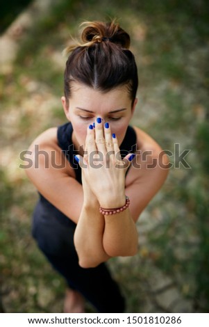 Top view of Caucasian  woman in sports wear standing on the ground in nature in eagle yoga pose. Selective focus on hands.
