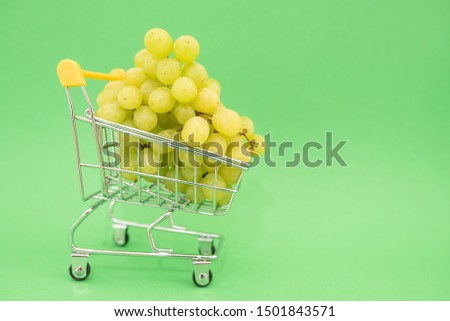 Mini shopping trolley on green background with grape, copy space, consumer concept, online shopping